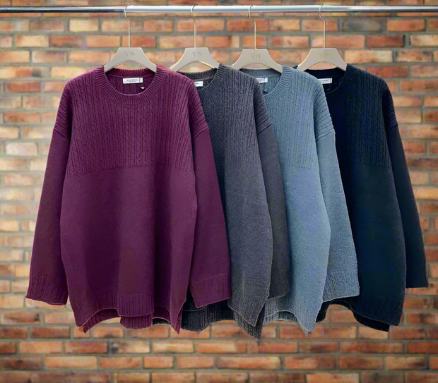 Three sweaters in purple, gray, and navy hanging on a rack against a white wall.